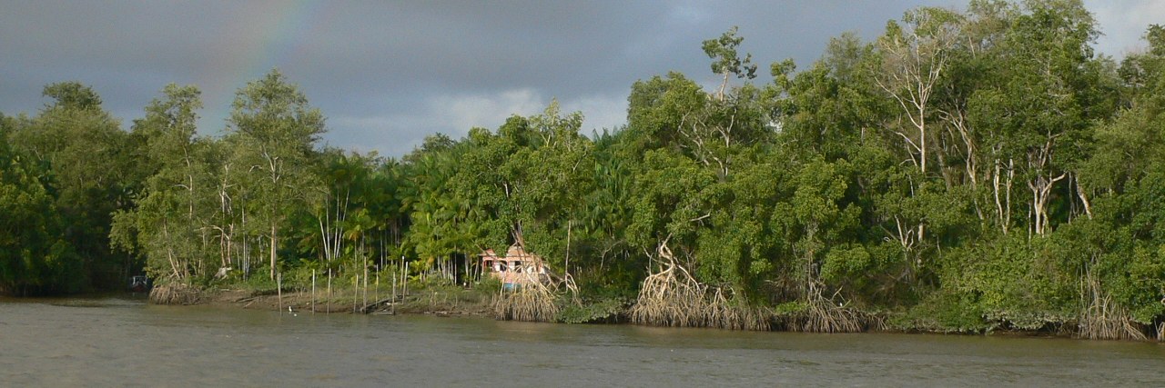 Rainbow over a river lined with mangrove forest in Pará, in the Brazilian Amazon, with a small house at the water's edge