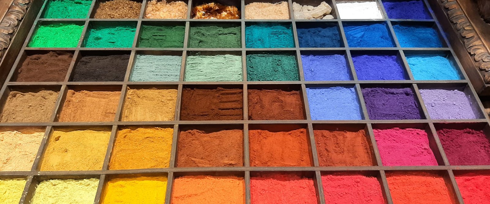 Wooden tray of colored pigment powders arranged in a grid