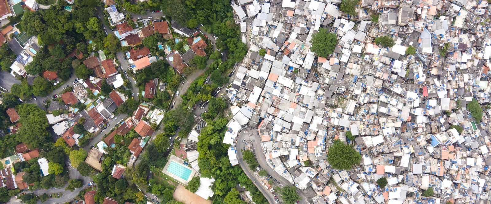 Aerial drone view of the border between the Rocinha favela and the Gávea neighborhood in Rio de Janeiro: dense rooftops on one side, houses with pools among trees on the other