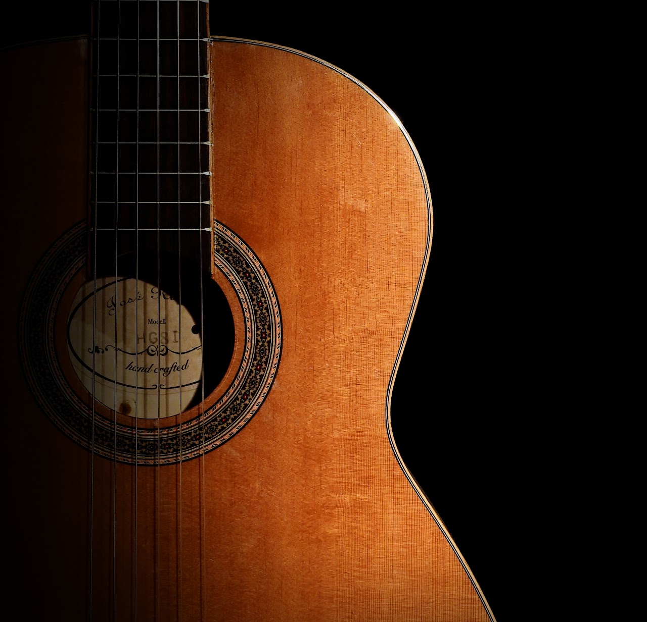 Close-up of an acoustic guitar body and sound hole on a black background