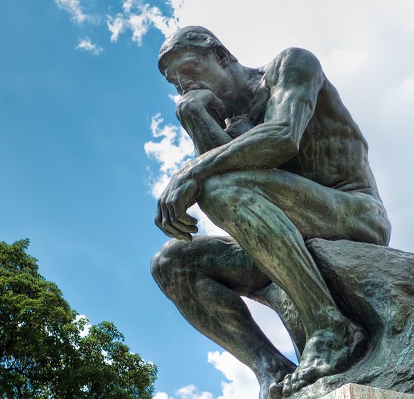 Bronze statue of The Thinker by Auguste Rodin against a blue sky